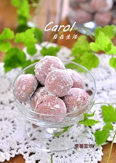 a glass bowl filled with powdered donuts on top of a wooden table next to green leaves