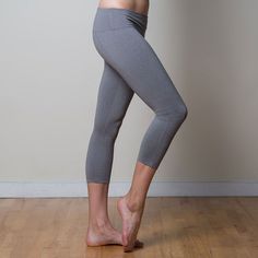 a woman standing on one leg with her hands behind her back, wearing grey yoga pants