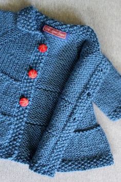 a blue knitted sweater with red buttons on the front and back, sitting on a white surface