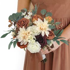 a woman holding a bouquet of flowers in her hands with brown and white blooms on it