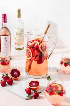 a pitcher filled with liquid and garnished with strawberries next to sliced oranges