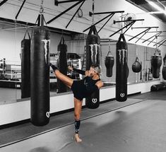 a woman is practicing her kickbox moves in a boxing gym with punching gloves hanging from the ceiling