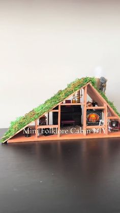 a miniature house made out of wood with grass on the roof and green roofing