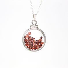 "Timeless handcrafted modern sterling silver genuine garnet shaker locket! This classic pendant is dime sized with coin style bezels, and clear lucite covers. The round charm hangs from a brand new sterling silver, and is filled with approximately 2.5 carats of round & cabochon cut faceted genuine garnet gemstones. An incredible piece of brand new gemstone jewelry, featuring January's birthstone! ERA - Brand New METAL / MATERIAL - Sterling silver locket & chain, lucite clear covers, 1 sc Silver Garnet Round Jewelry, Round Silver Garnet Jewelry, Silver Garnet Birthstone Necklace, Faceted Sterling Silver Gemstones As Gifts, Garnet Birthstone Round Necklace, Faceted Round Gemstones For Gift, Round Faceted Gemstones For Gifts, Round Garnet Gemstone Necklaces, Red Sterling Silver Gemstones