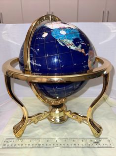 a blue and gold globe sitting on top of a metal stand next to a ruler