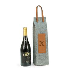 a bottle of wine sitting next to a bag on a white surface with a brown leather handle