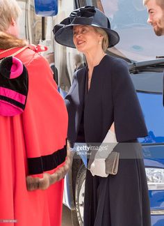 two women in hats talking to each other near a blue car and another woman wearing a red dress