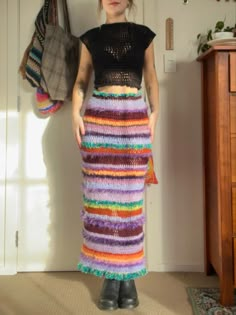 a woman standing in front of a wall wearing a multicolored knitted skirt