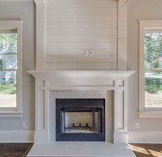 an empty living room with a fireplace in the center and two windows on either side