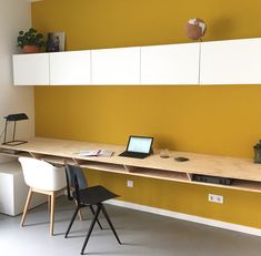 a laptop computer sitting on top of a wooden desk in front of a yellow wall