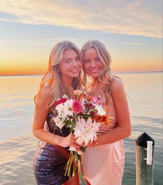 two beautiful young women standing next to each other near the ocean holding flowers in their hands