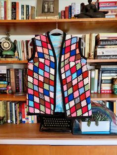 a colorful vest is hanging on a book shelf next to a typewriter and books