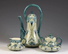 three pieces of pottery are sitting on a white tablecloth and one is green with blue flowers