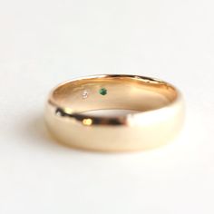 a gold wedding band with two diamonds on the top and one green stone in the middle