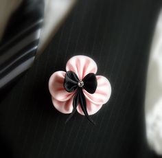 a pink and black flower on a black suit lapel pin with a white stripe tie