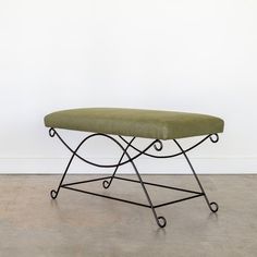 a green bench sitting on top of a metal frame in front of a white wall