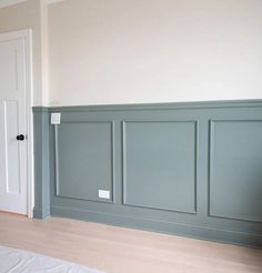 an empty room with wood flooring and gray paneling on the walls, along with a white door