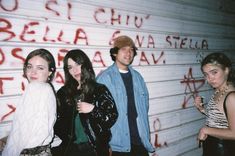 four people standing in front of a wall with graffiti on it