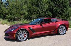 a red sports car is parked on the side of the road in front of some trees