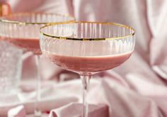 two glasses filled with pink liquid sitting on top of a white cloth covered tablecloth