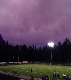 a football field with people standing on it under a purple sky and some dark clouds