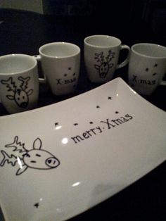 six coffee mugs and a plate with merry xmas written on them sitting on a table