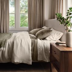 a bed with pillows and blankets in a bedroom next to a window filled with potted plants