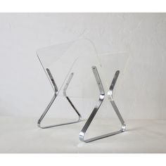 two clear acrylic chairs sitting side by side on a white surface with one chair facing the other