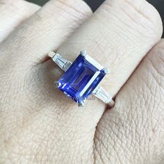 a woman's engagement ring with an emerald and baguette cut blue sapphire