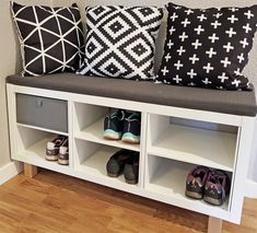 some pillows and shoes are sitting on a bench in front of a wall with white shelves