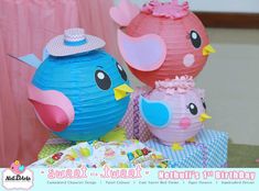 two paper birds sitting next to each other on top of a table with pink and blue decorations