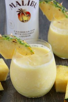 two glasses filled with pineapple drink next to slices of pineapple