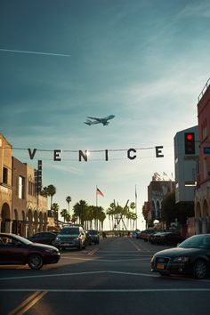 an airplane is flying over the street with cars parked on the side walk and palm trees