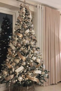 a christmas tree with gold and silver ornaments in a living room next to a window