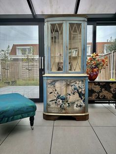 a blue cabinet sitting in the middle of a living room next to a chair and ottoman