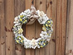 a white wreath with yellow and white flowers hanging on a wooden wall next to a door