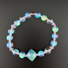 Mystic Aura Quartz beaded stretch bracelet featuring glass accent beads, rose gold-finished glass spacer beads, and mood bead focal. With flashes of blue and a color-changing mood bead, this unique stretch bracelet is sure to mesmerize you with all the different shades of the rainbow. The bracelet measures 6.5 inches and fits a wrist size of 6.5 inches with a bit of wiggle room. Use a rolling motion when putting on your stretch bracelet. Spiritual Iridescent Beaded Bracelets, Iridescent Bracelets With Faceted Beads, Czech Glass Stretch Bracelet With Spacer Beads, Spiritual Hand-strung Czech Glass Stretch Bracelet, Adjustable Iridescent Beaded Stretch Bracelet, Aura Quartz, Beaded Stretch Bracelet, Stretch Bracelet, The Rainbow