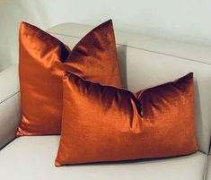 two orange pillows sitting on top of a white couch