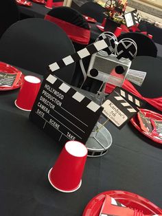 a black table topped with red plates and movie clapperboard decorations on top of it