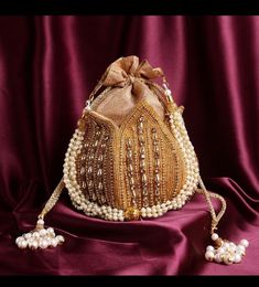 a small purse with pearls on it and a brown ribbon around the handle, sitting on a purple cloth