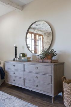 a bedroom with a bed, dresser and large round mirror on the wall above it