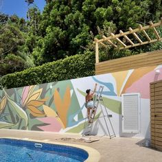 a man painting a mural on the side of a wall next to a swimming pool