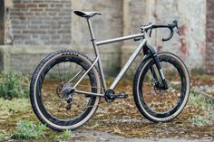 a silver bike parked in front of an old brick building with grass and weeds on the ground