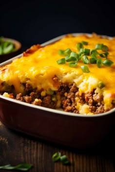 a casserole dish with meat, cheese and green onions in it on a wooden table