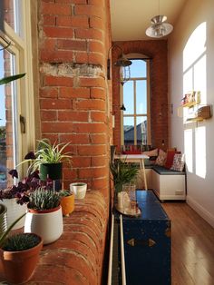 a brick wall with potted plants on the window sill next to a couch