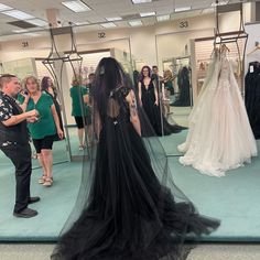 a woman in a black dress is looking at herself in the mirror while others look on