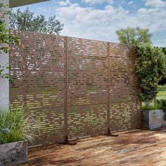 a large wooden fence on top of a wooden deck next to a tree and bushes