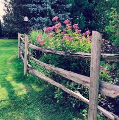 a wooden fence with flowers growing on it in the middle of a grassy area next to trees and bushes