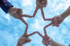 four hands making a star shape with their fingers in the middle, against a blue sky background