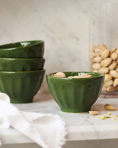 three green bowls sitting on top of a counter next to cashews and nuts